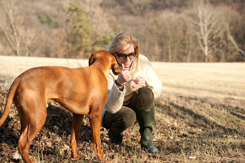 Objektsuche Hundetraining Wolfgangsee. Frauchen hockelt neben ihrem Hund und zeigt mit dem Daumen nach oben, weil ihr Hund das verlorene Objekt gefunden hat